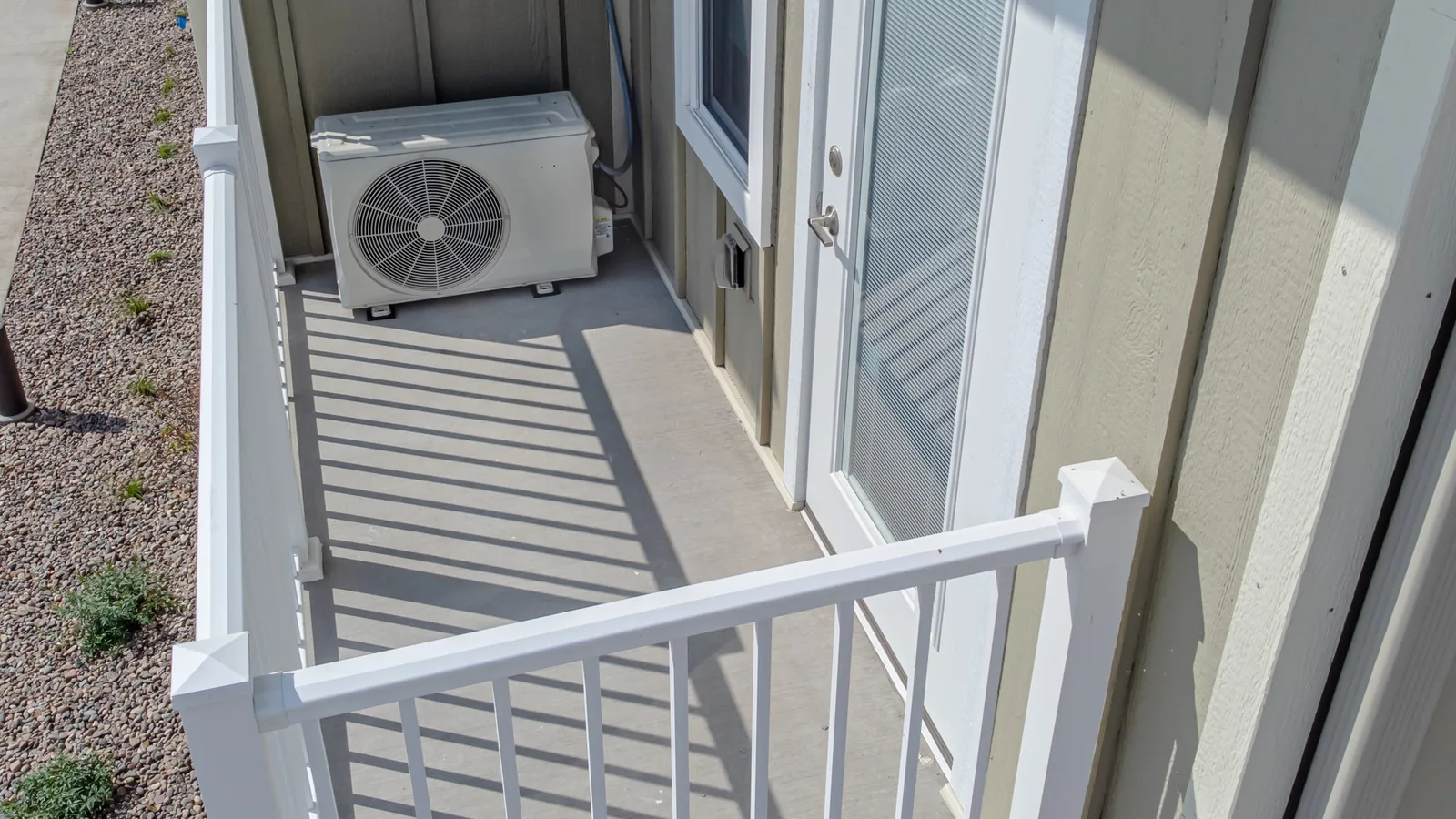 White mini split outdoor condenser unit on a concrete pad beside a small beige building with stairs, a mini split for shed setup