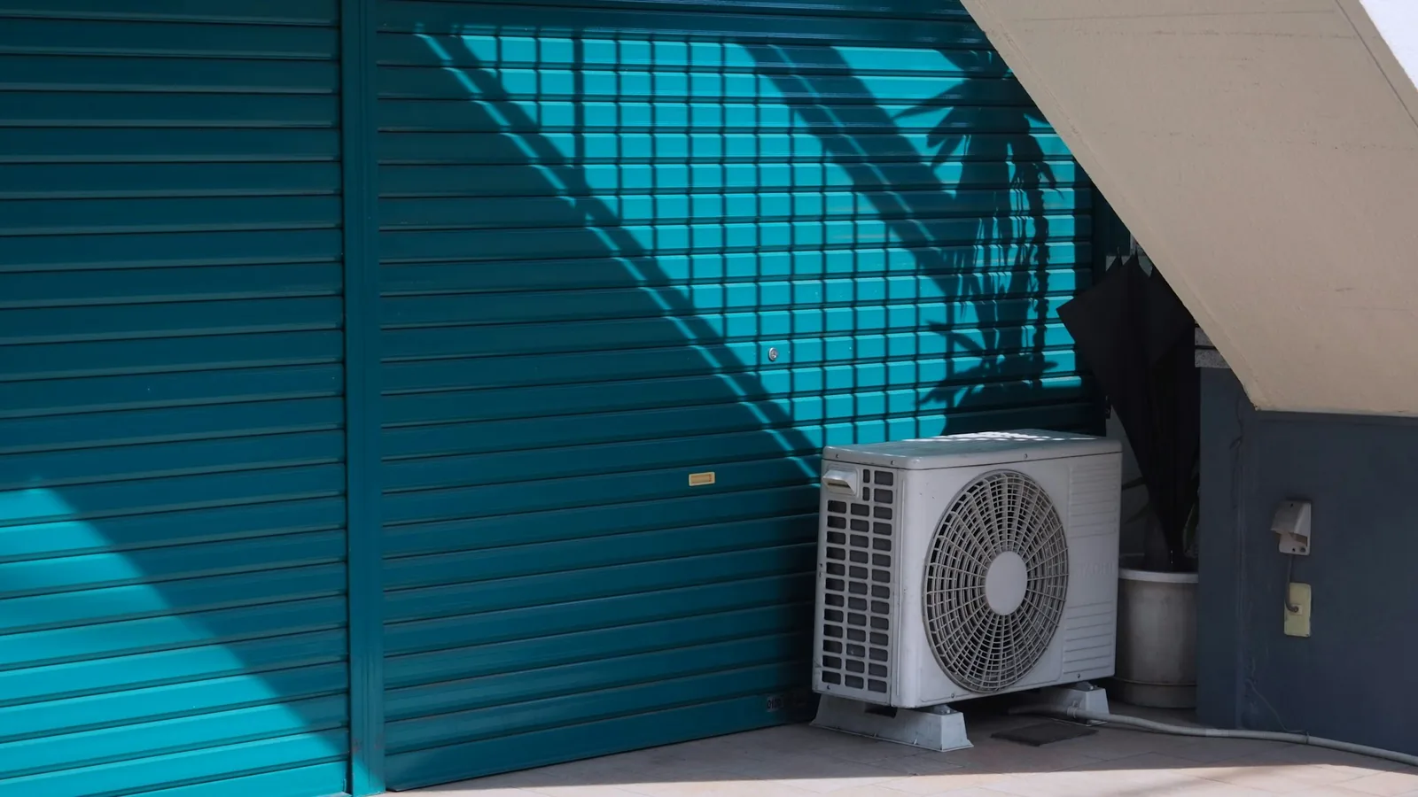 White mini split for workshop best outdoor condenser unit on concrete floor beside teal corrugated metal door with overhead staircase