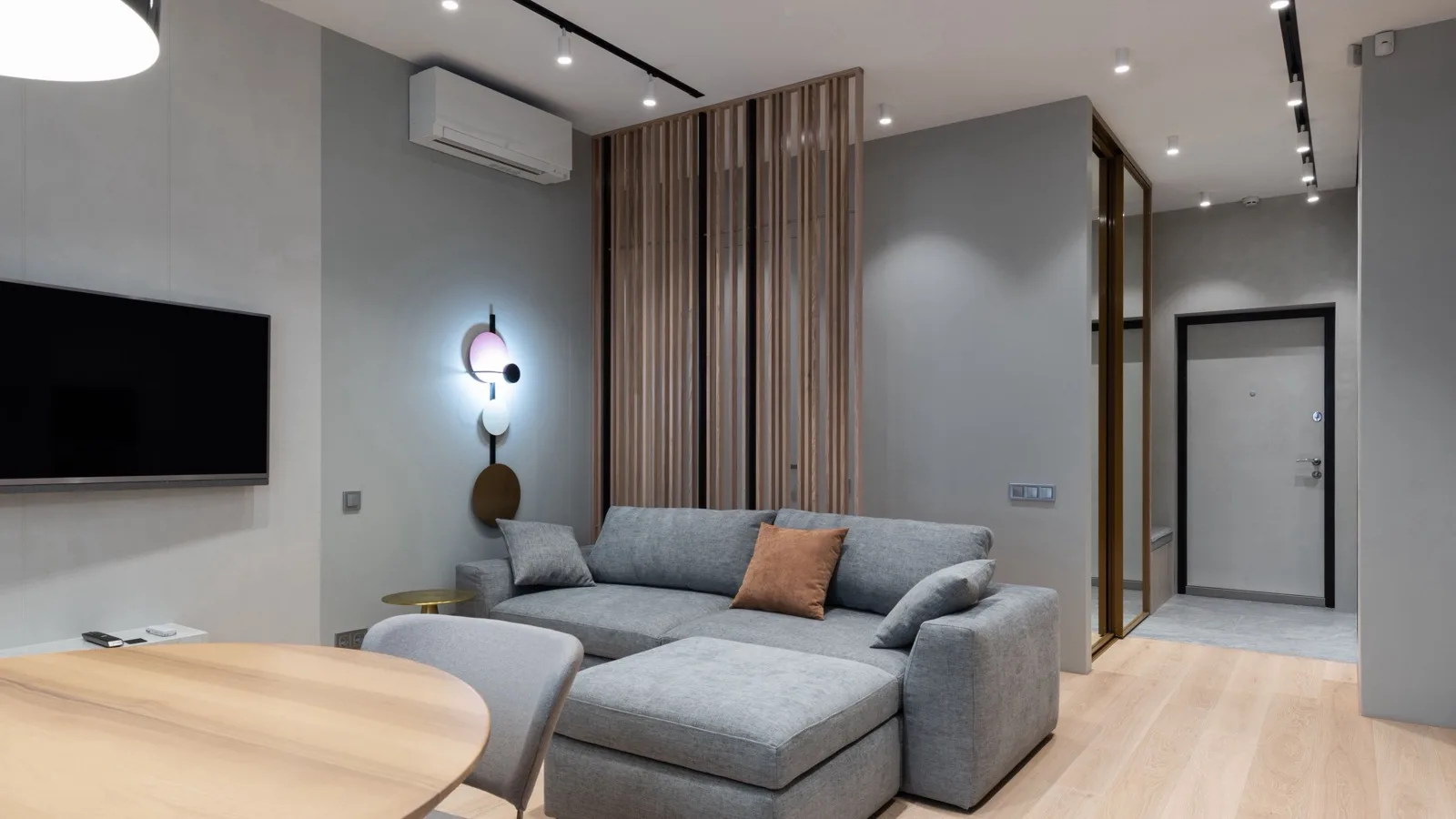 Modern open-plan living room with a white wall-mounted ductless mini split above a gray sectional sofa, the kind of 500 sq ft space a 12,000 BTU DIY mini split is sized for