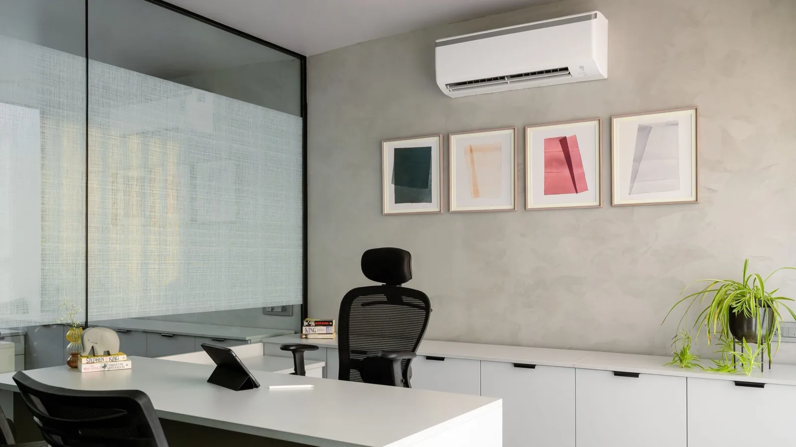 White wall-mounted ductless mini split above framed prints in a small home office with a white desk and black mesh chair, a 250 sq ft room suited to a 9,000 BTU DIY mini split