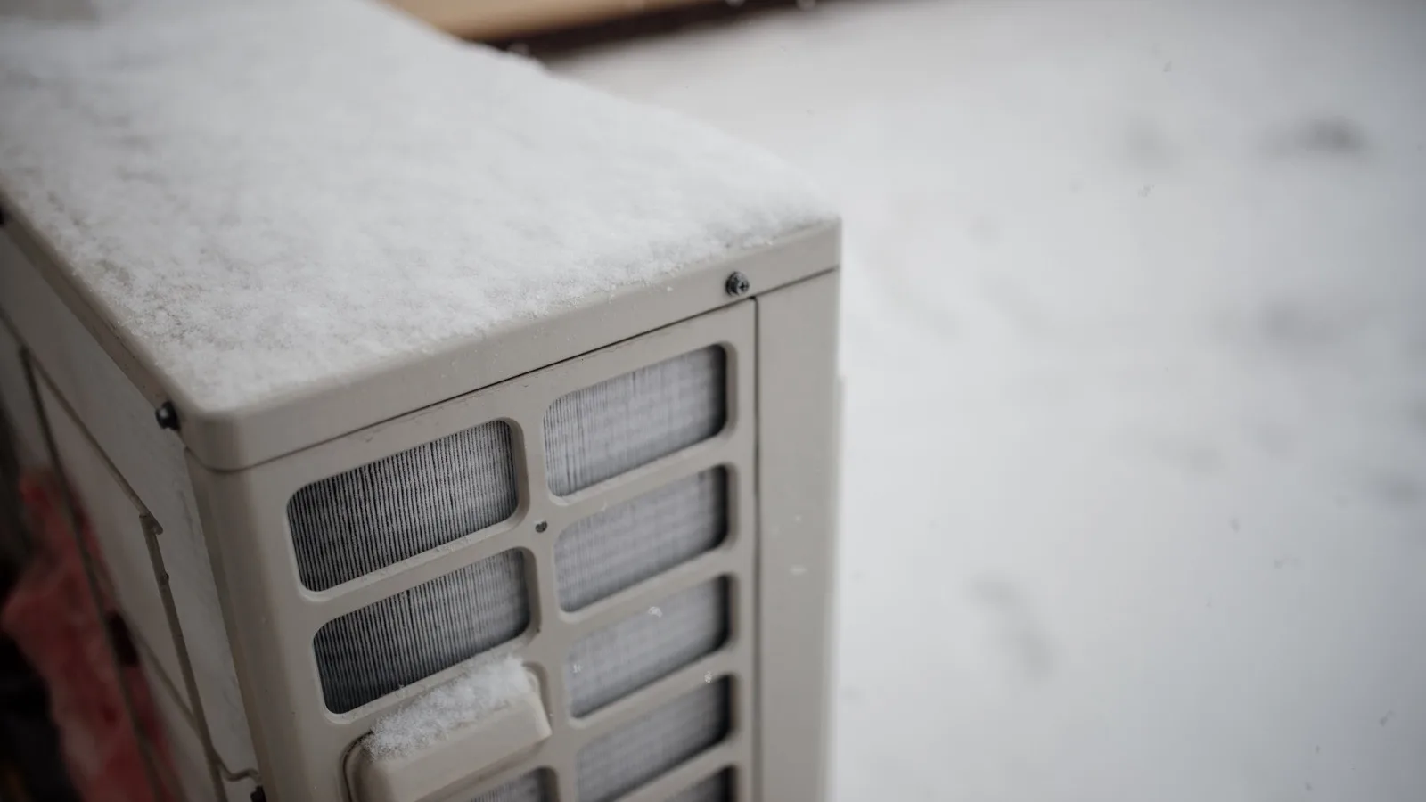 Snow-covered outdoor condenser of a ductless mini split heat pump during a winter snowfall, illustrating cold-climate heating in the MRCOOL DIY vs competitors comparison
