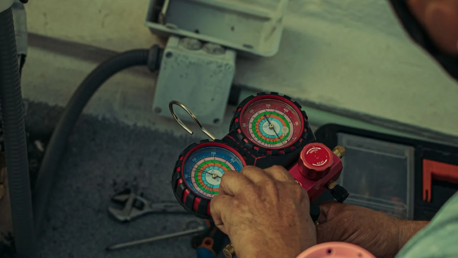 HVAC technician holding a refrigerant manifold gauge set with red and blue pressure gauges and a charging hose while servicing an air conditioning system — the regulated refrigerant work that requires EPA Section 608 certification
